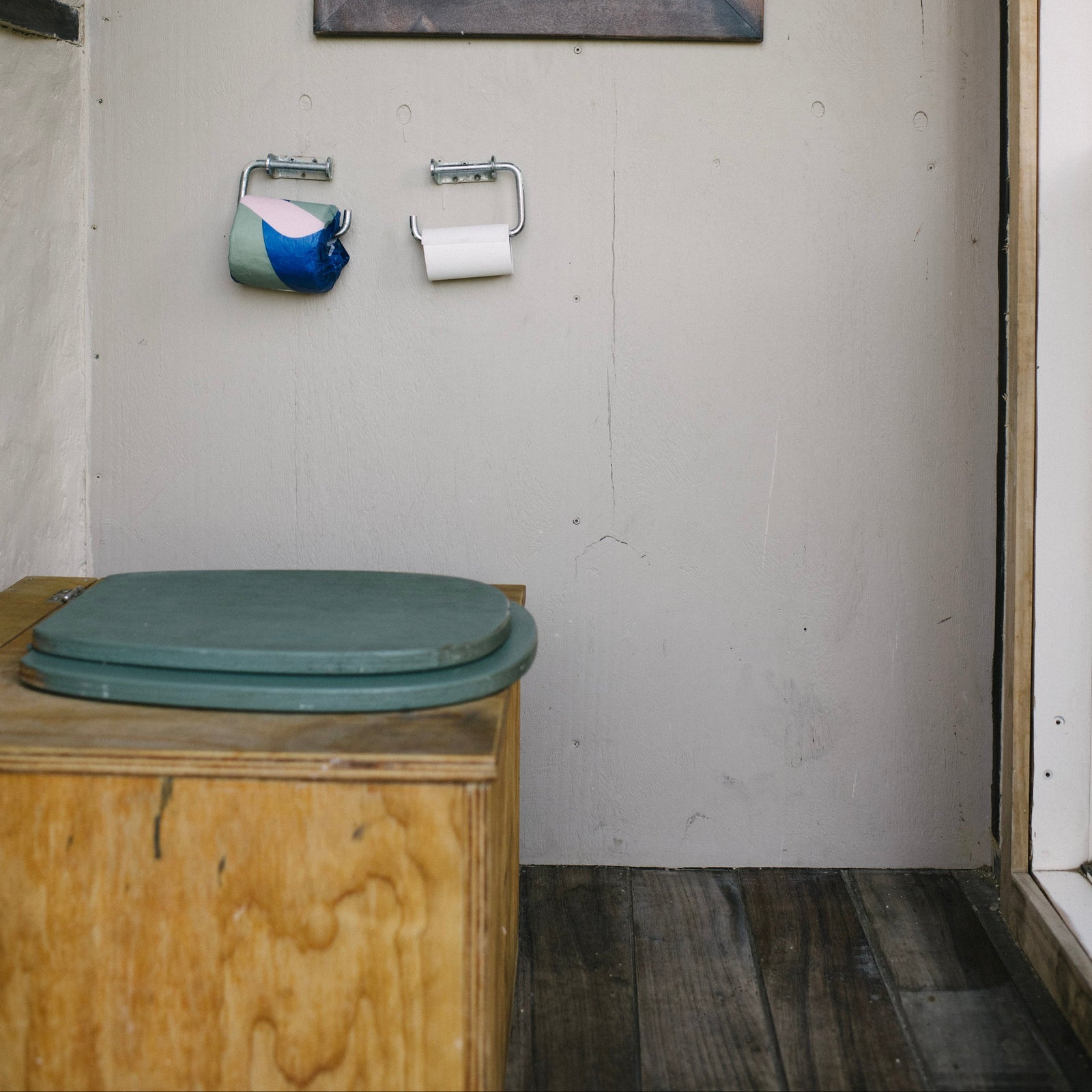 Wooden composting toilet with a framed picture on the wall in a bathroom setting.