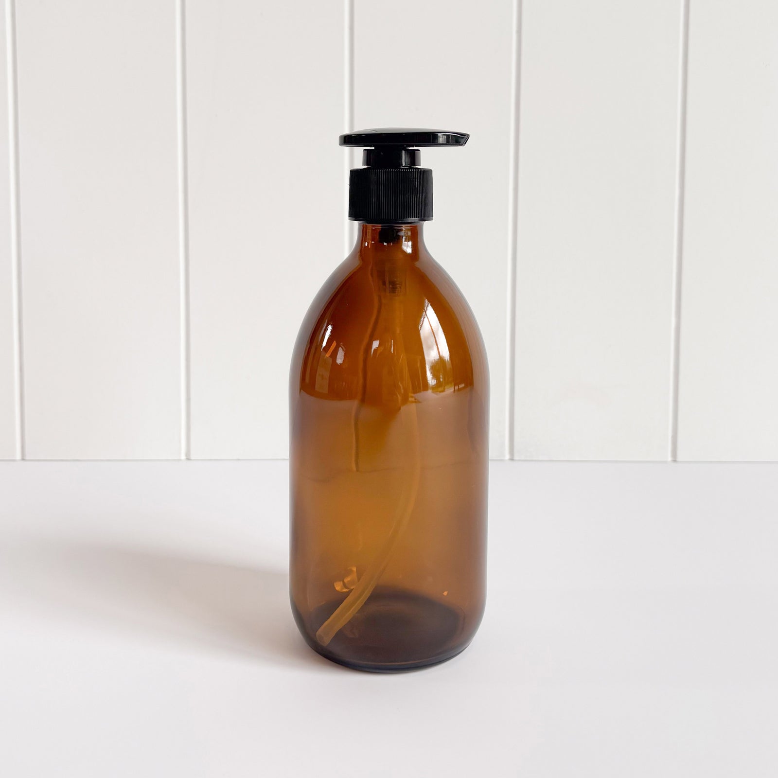A person's hands using a dark amber glass pump bottle filled with liquid, presumably hand soap or sanitizer, at a sink.