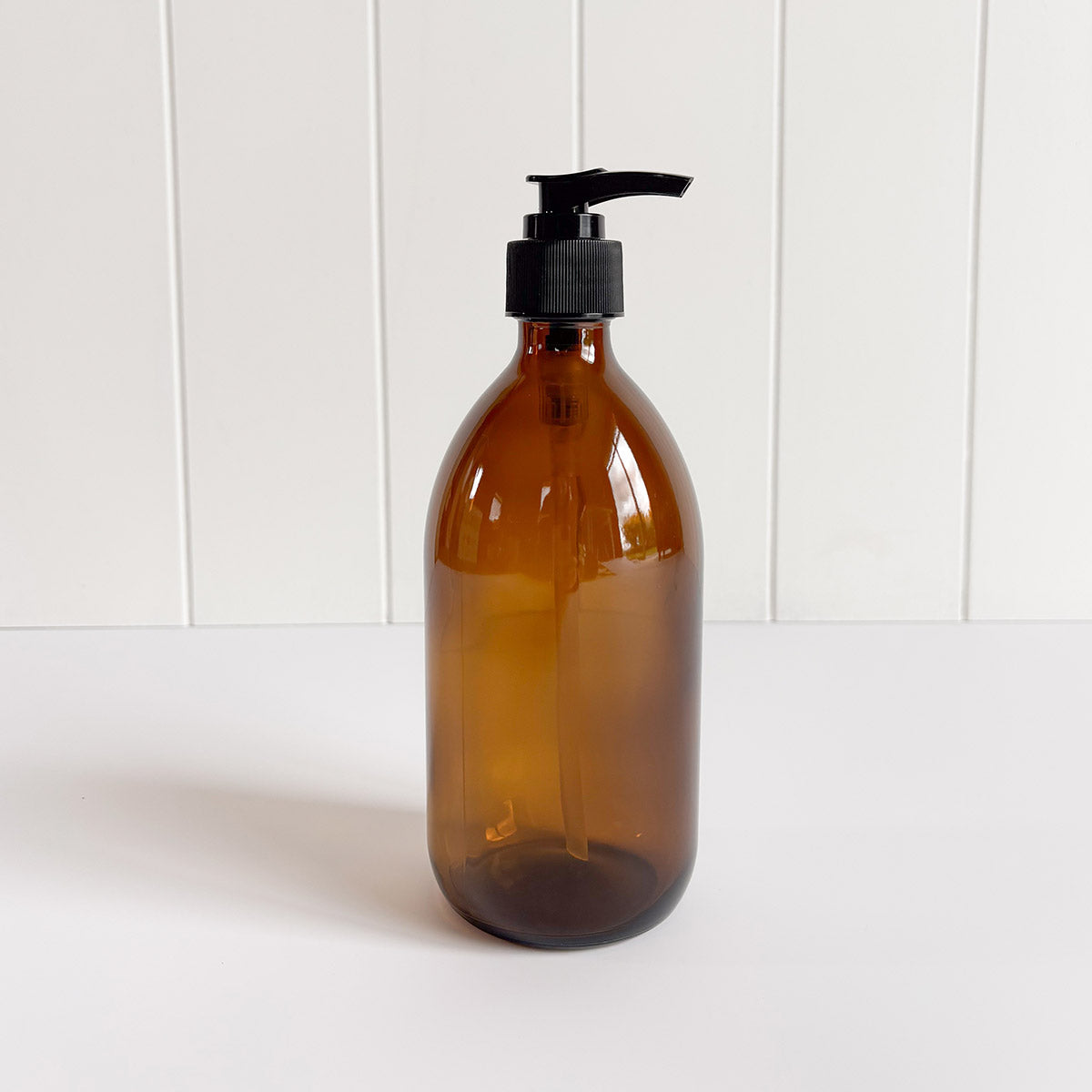 A person's hands using a dark amber glass pump bottle filled with liquid, presumably hand soap or sanitizer, at a sink.