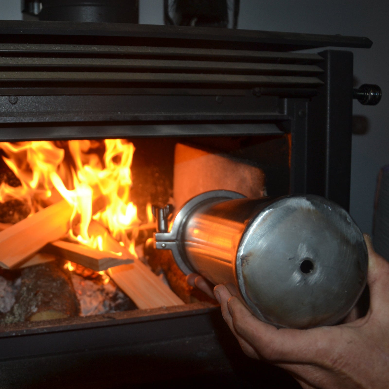 Person using a metal tool to tend to a fire in a wood stove.