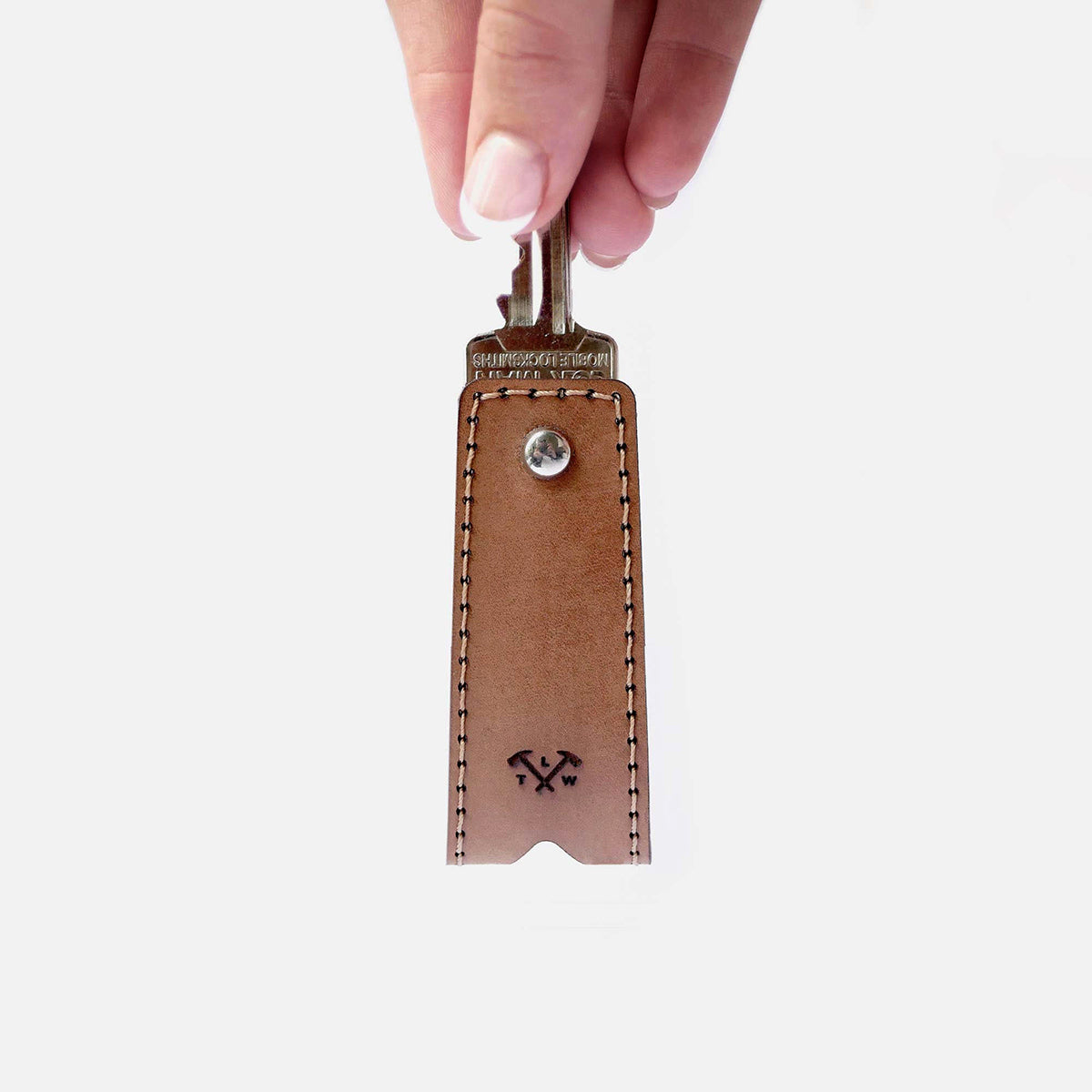 Brown leather keychain with stitching detail held by a hand on a light gray background