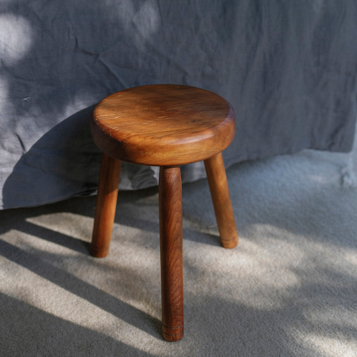 Wooden milking stool with a three legs on a textured gray surface in the bedroom