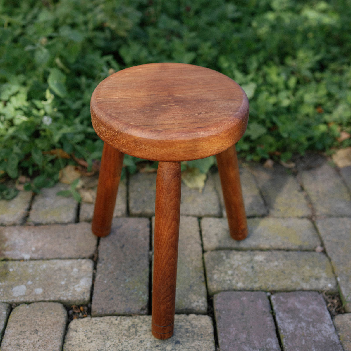 Wooden small stool on a paved surface with greenery in the background