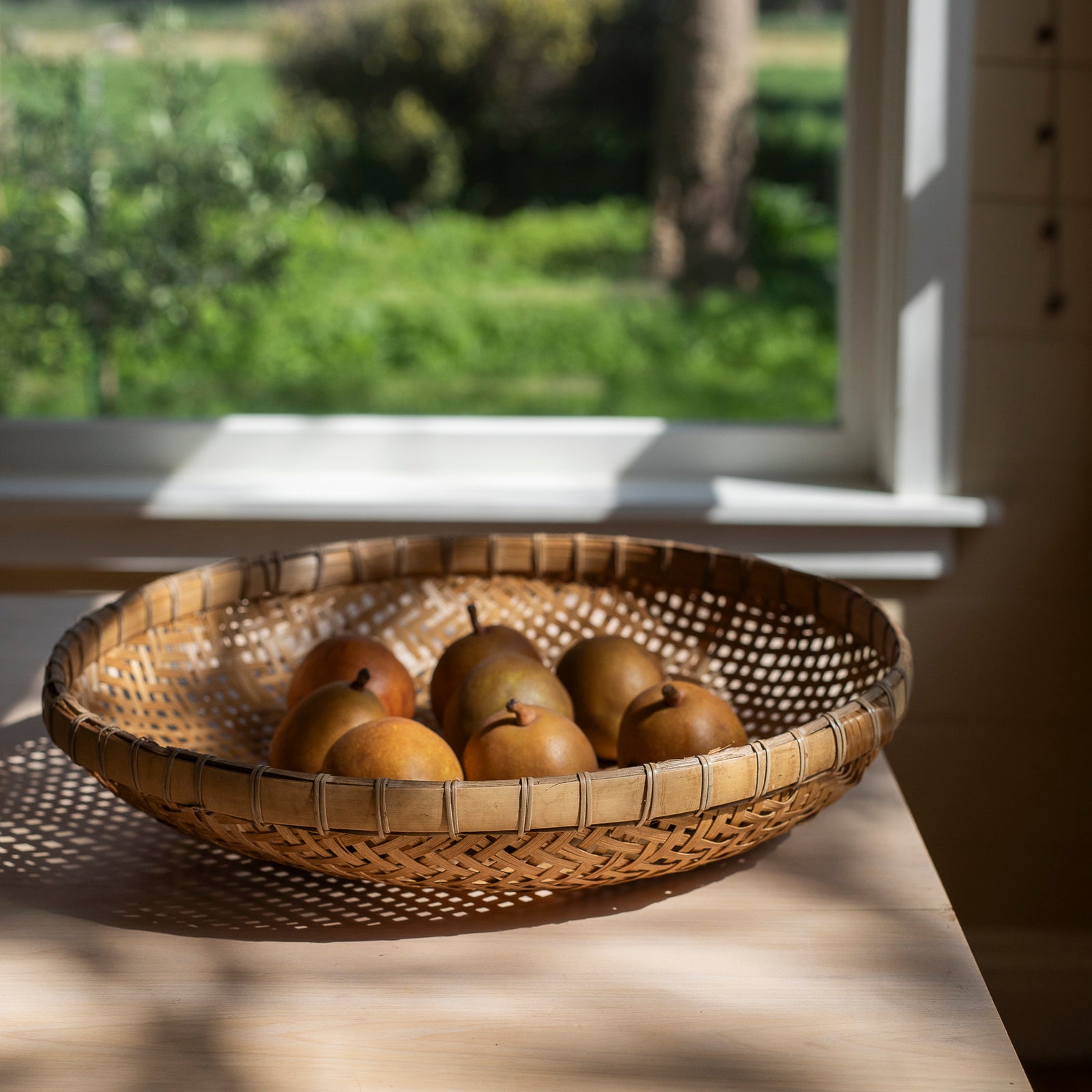 Woven bamboo basket with pears on a windowsill with a garden view. Fruit bowl.