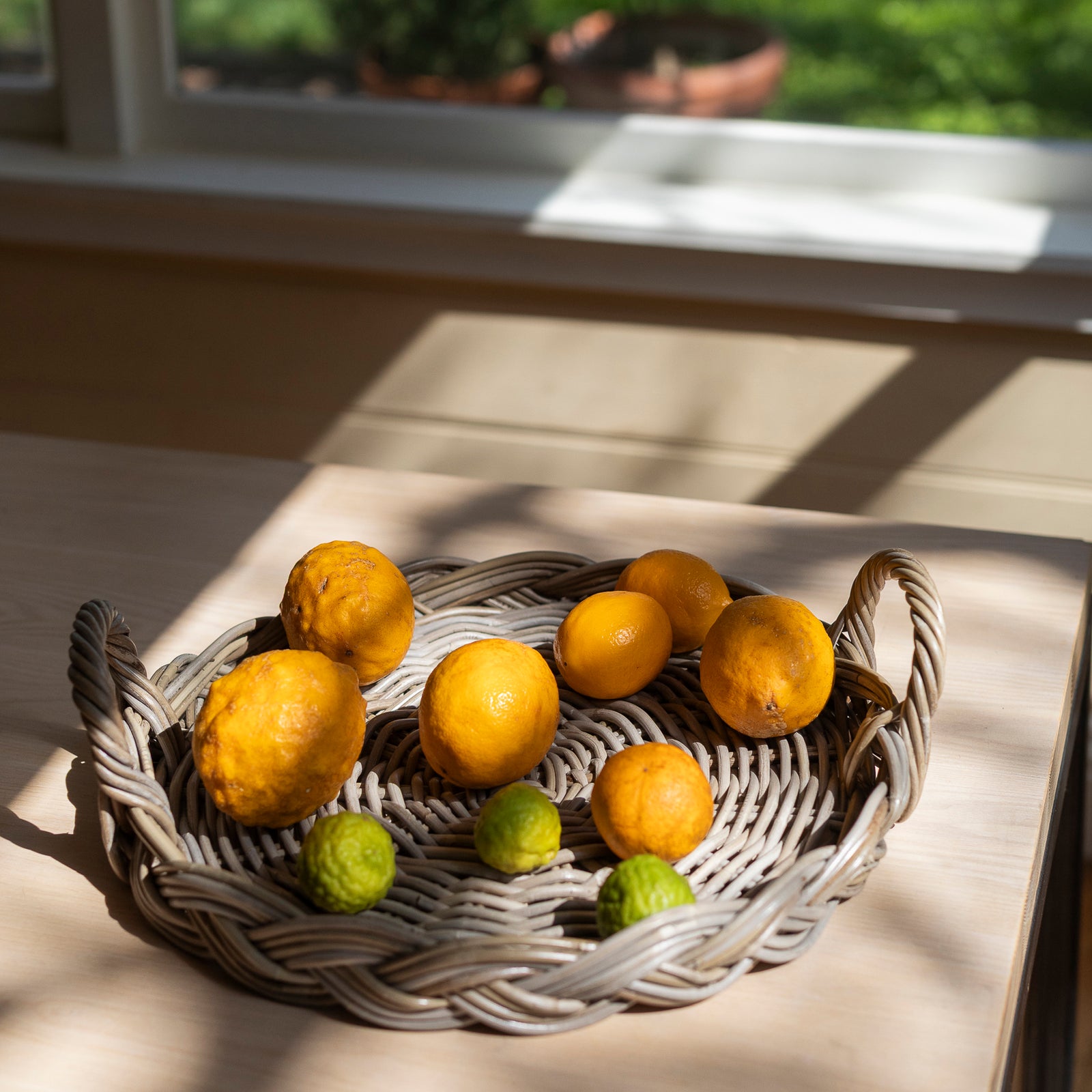 Wicker tray basket with lemons and limes on a wooden surface near a window