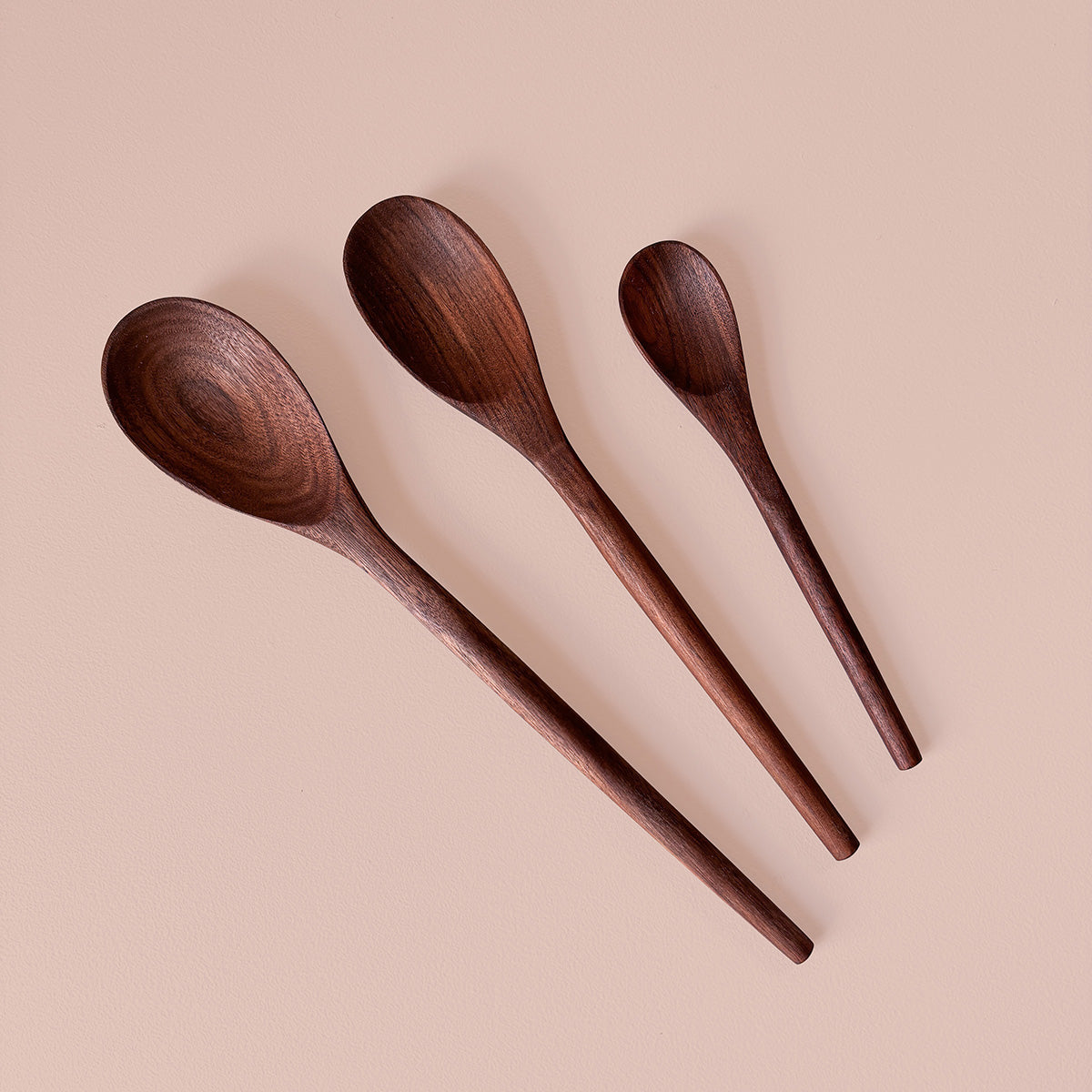 Three wooden spoons made from black Walnut on a beige background.