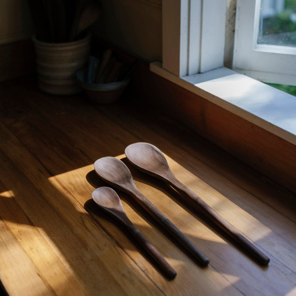 Three wooden spoons on a wooden surface with sunlight streaming in from a window.