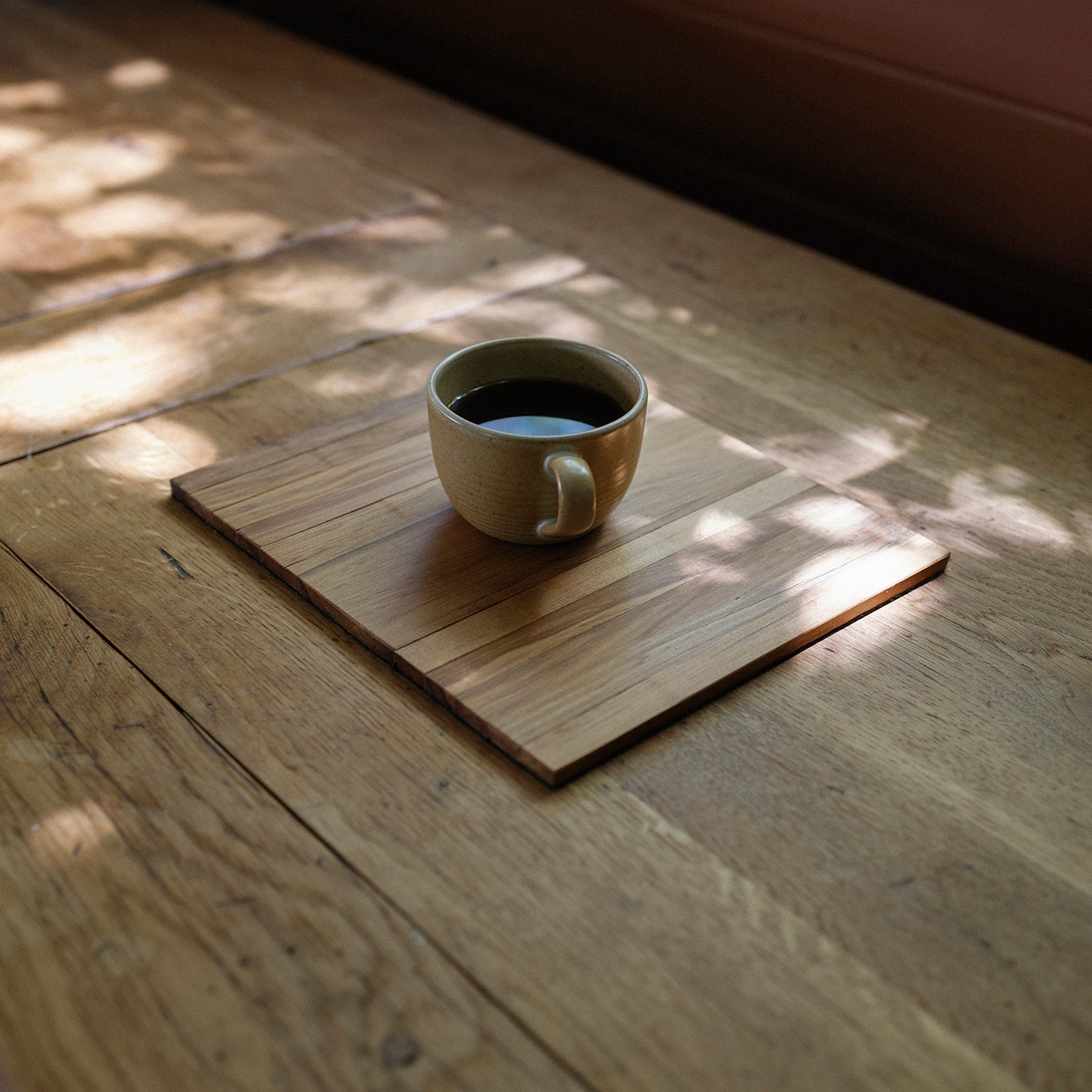 Ceramic cup of coffee on a wooden coaster with sunlight filtering through leaves