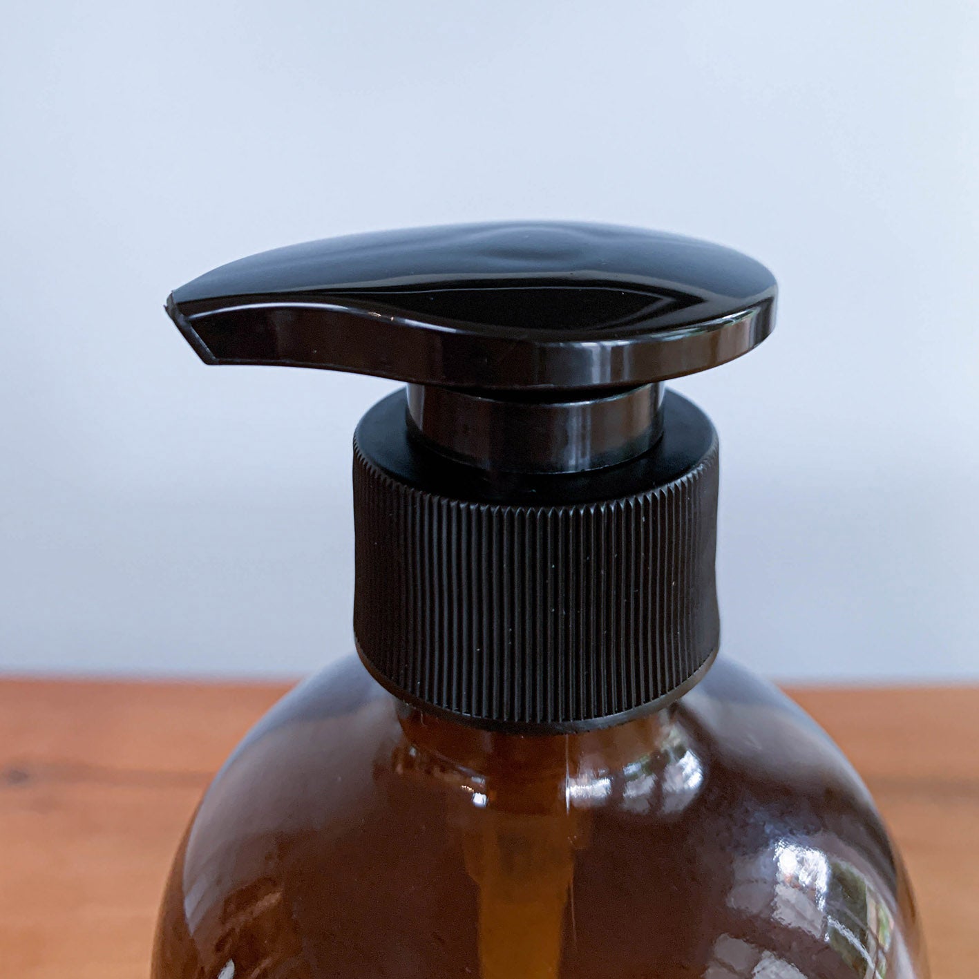 A person's hands using a dark amber glass pump bottle filled with liquid, presumably hand soap or sanitizer, at a sink.