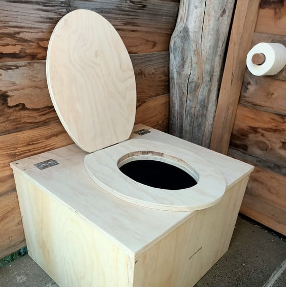 Wooden composting toilet with a wooden seat on a stone floor.