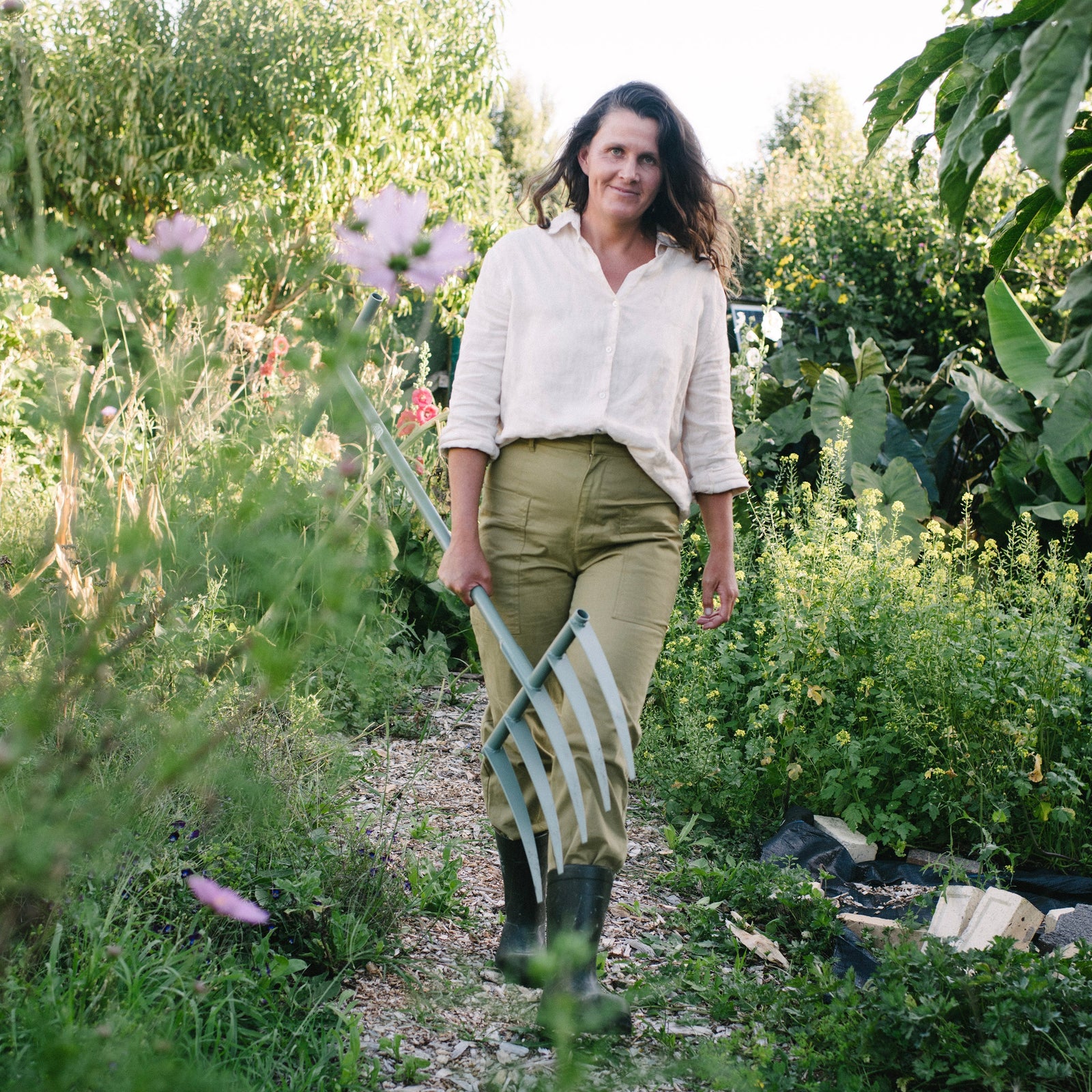 Woman walking through a garden holding gardening tools
