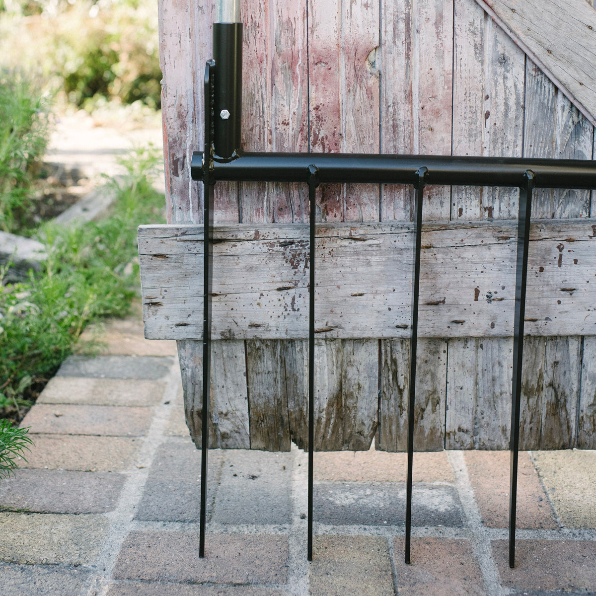 Metal garden trellis against a wooden wall with a blurred natural background