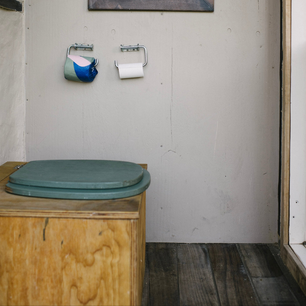 Wooden composting toilet with a framed picture on the wall in a bathroom setting.