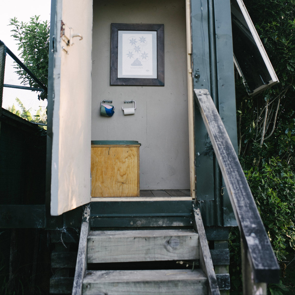 Small wooden shed with open door, steps leading up to it, and a composting toilet inside.