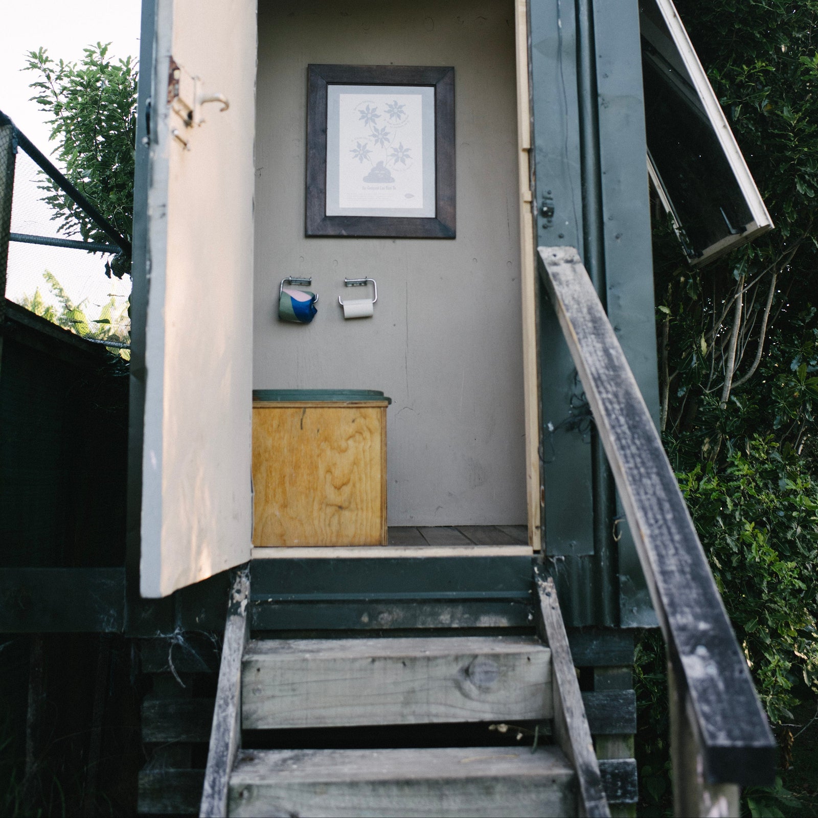 Small wooden shed with open door, steps leading up to it, and a composting toilet inside.
