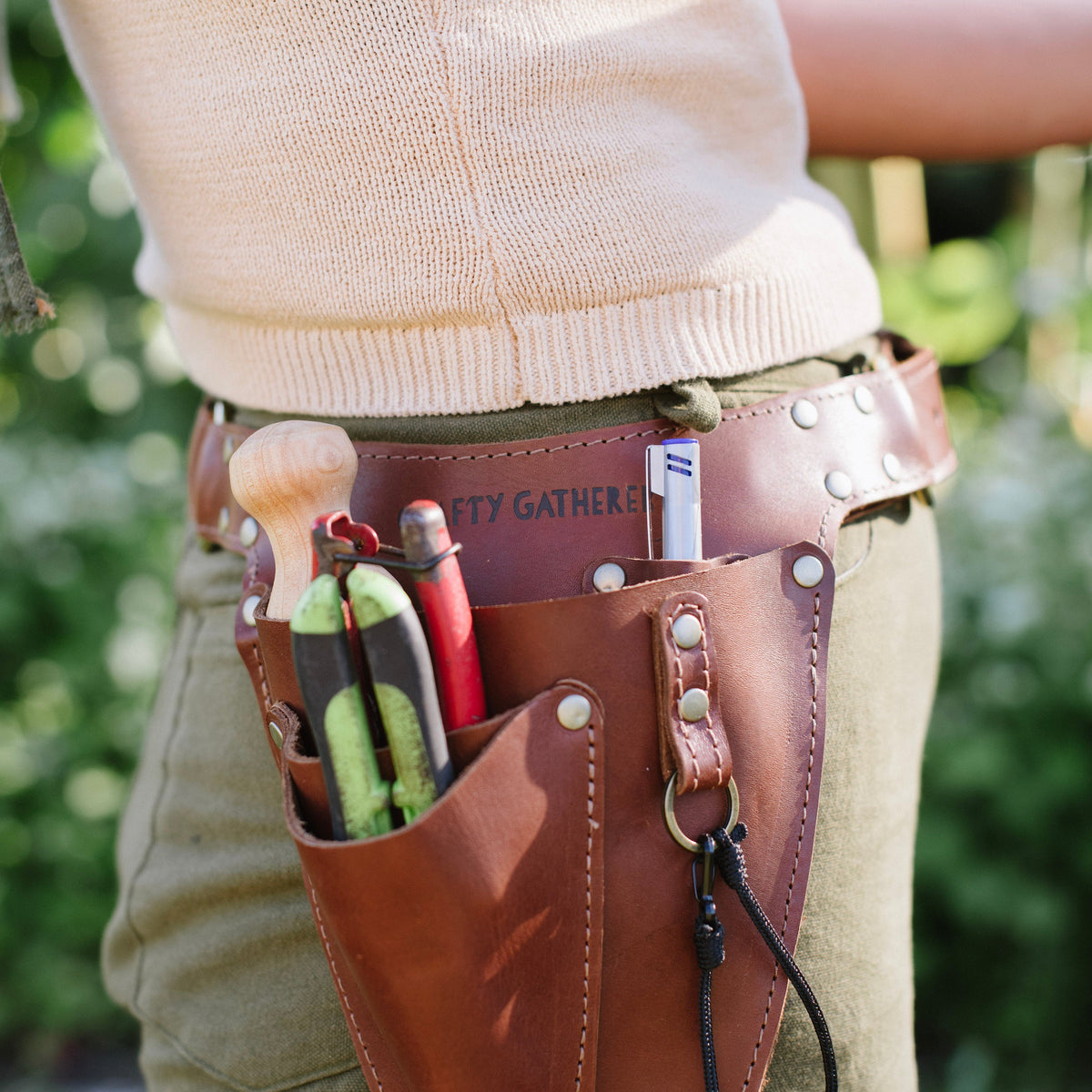 Person wearing a brown leather tool belt with various items against a blurred green background