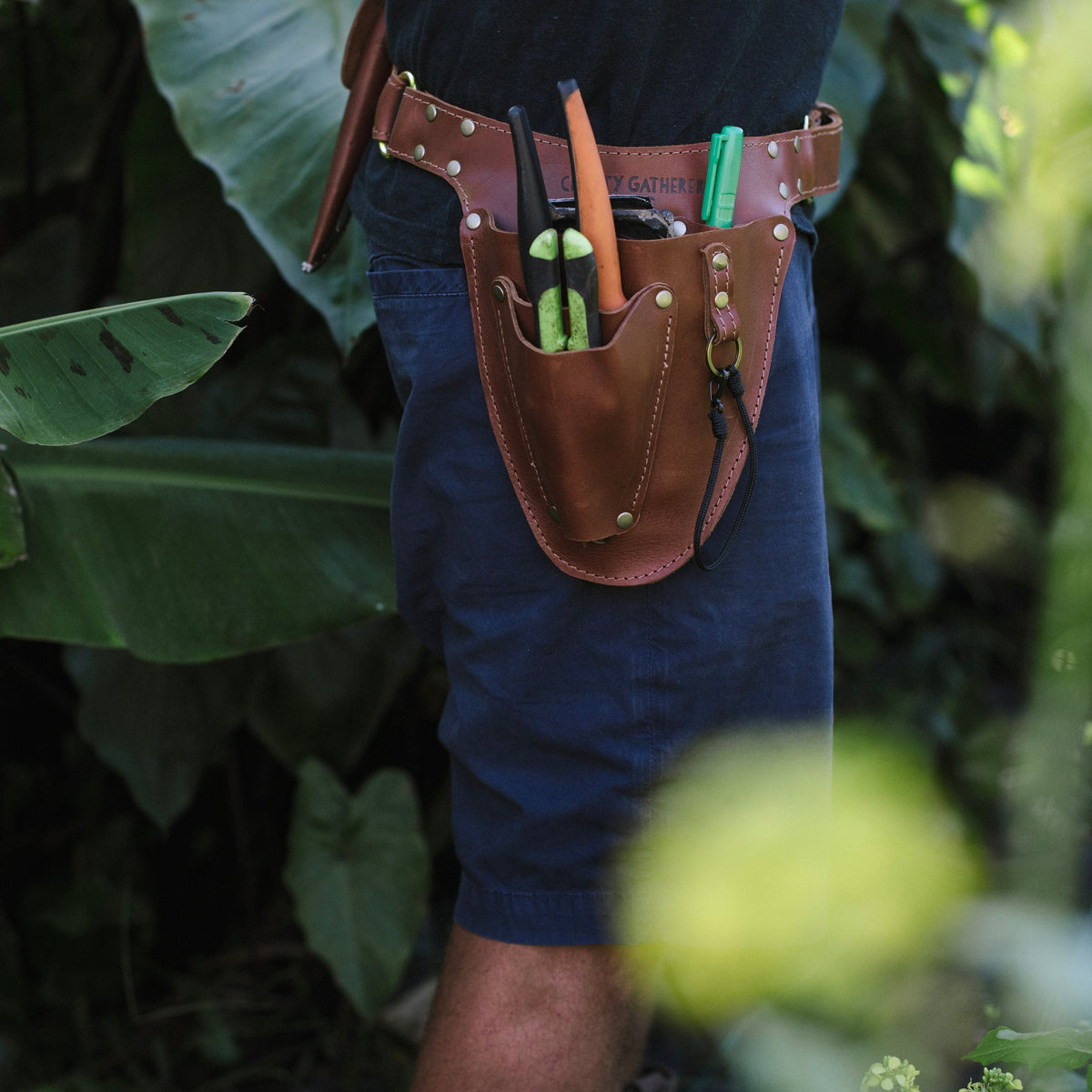 Person wearing a leather tool belt with various tools in a natural setting