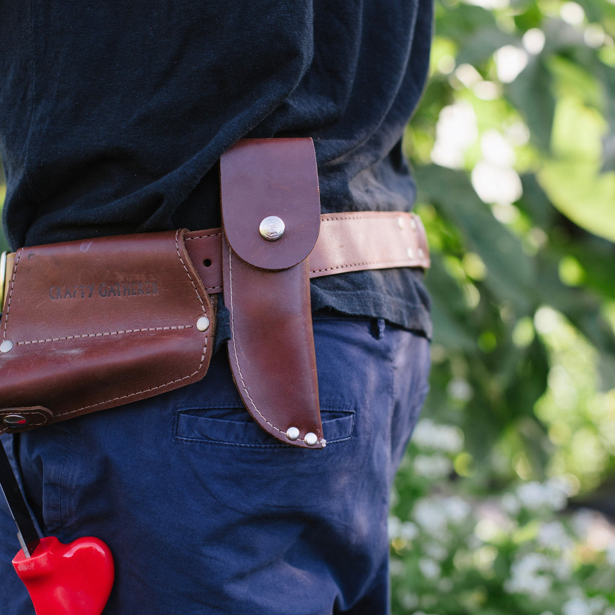 Person wearing a brown leather tool belt with a red tool against a blurred green background