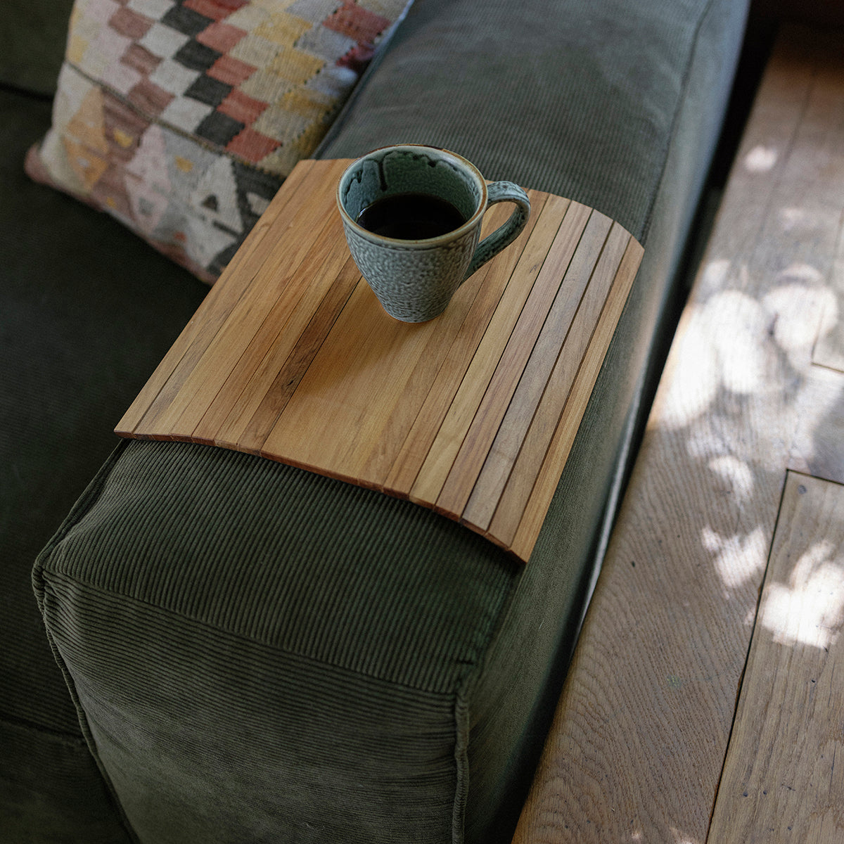 Mug on a wooden arm rest tray attached to a sofa arm