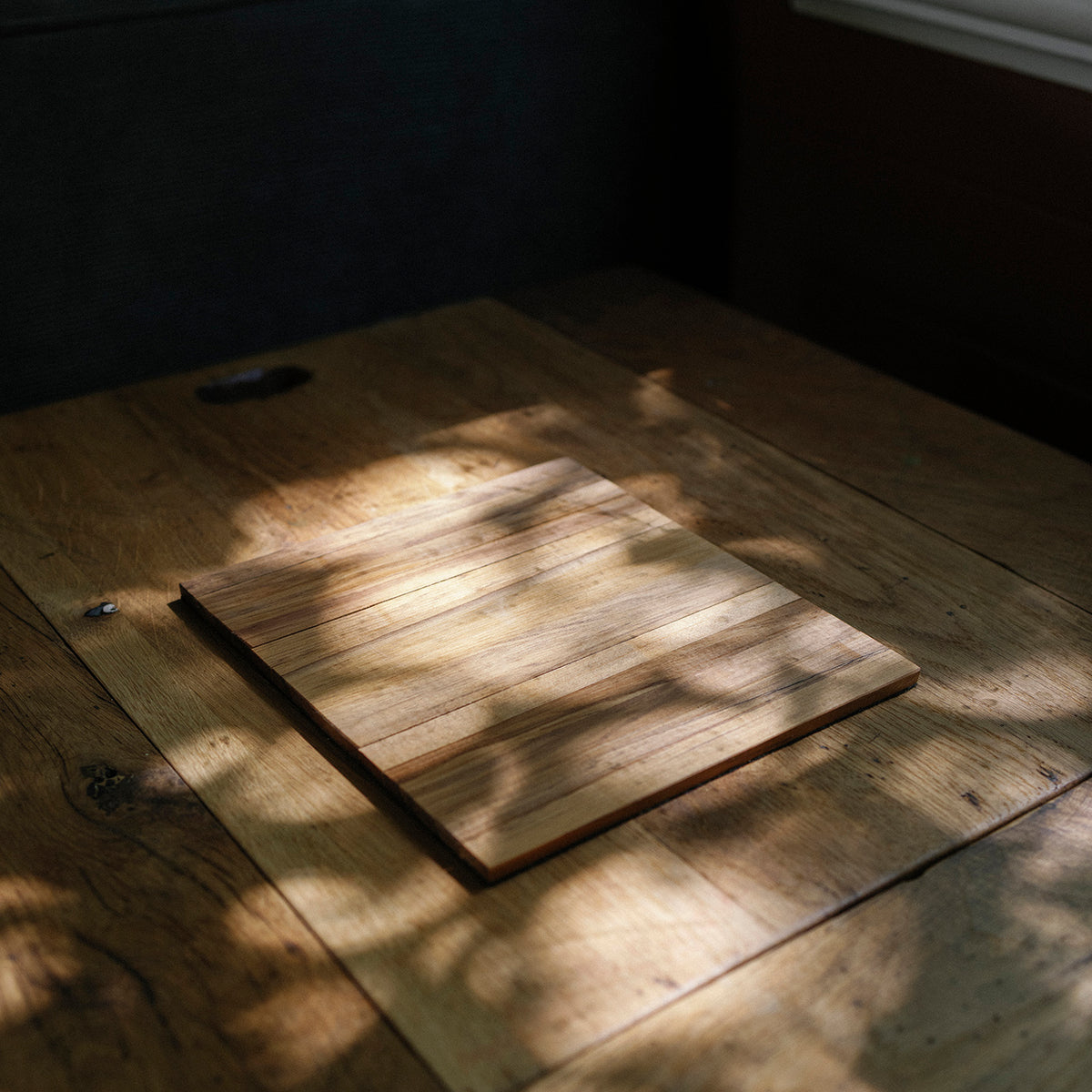 Wooden cutting board on a wooden table with sunlight casting shadows