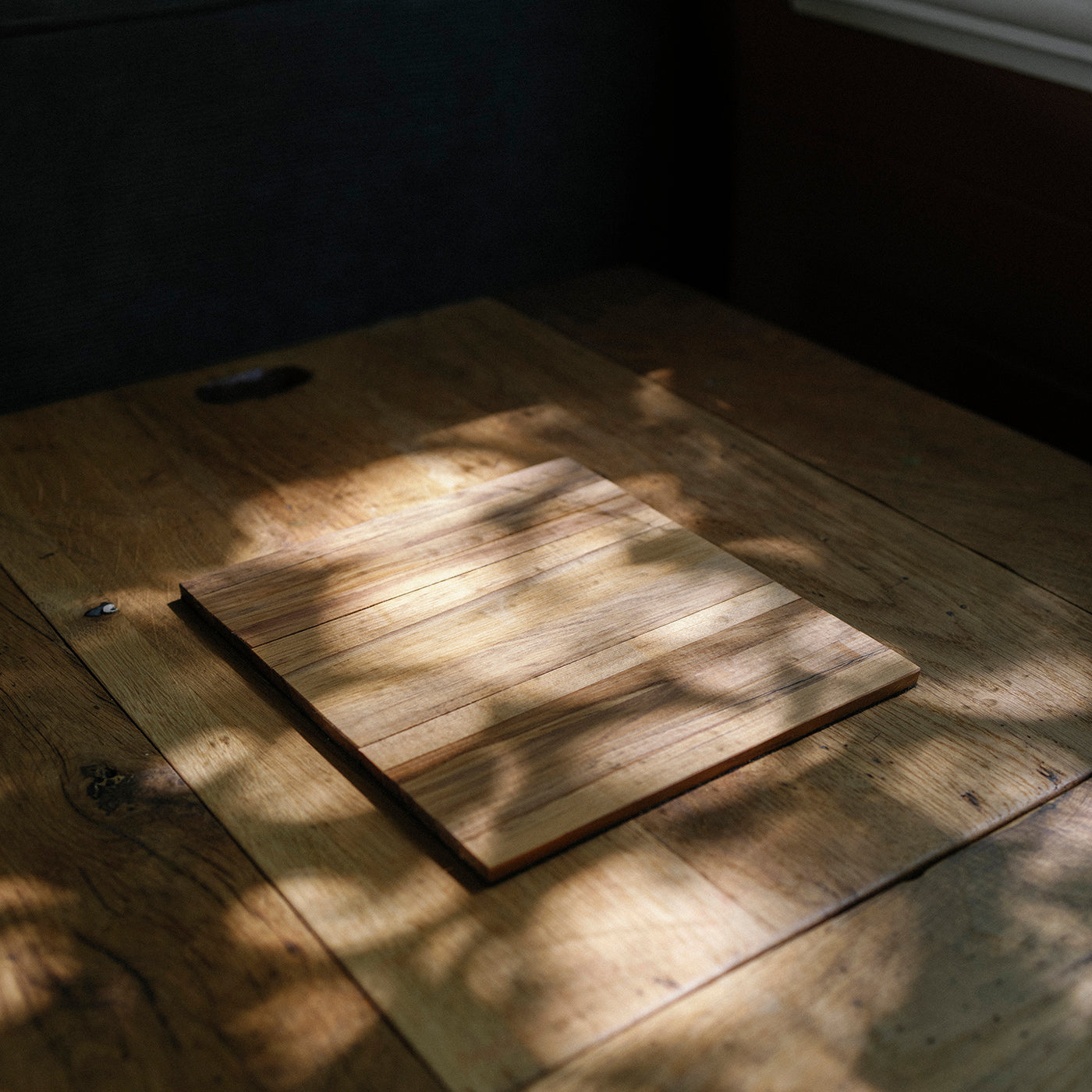 Wooden cutting board on a wooden table with sunlight casting shadows
