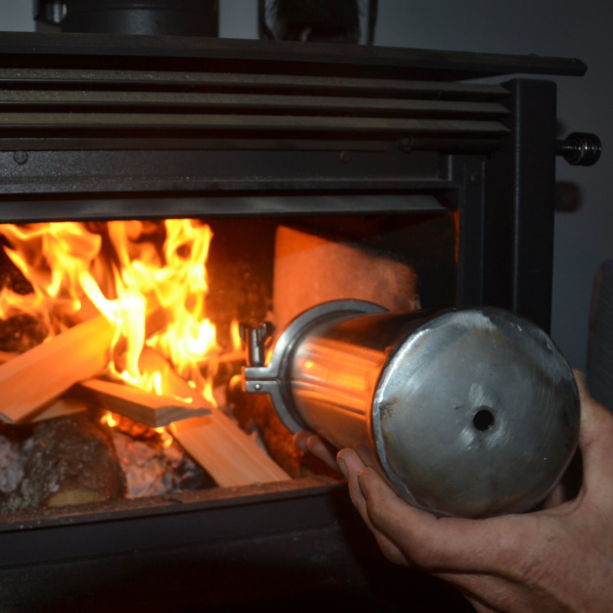 Person using a metal tool to tend to a fire in a wood stove.