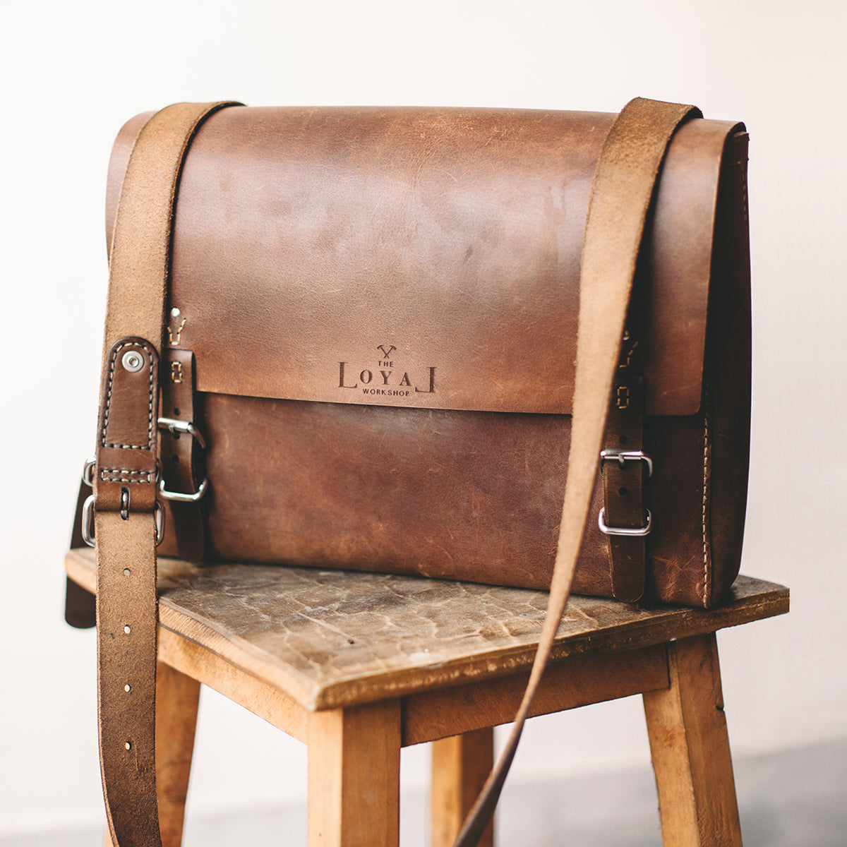 Brown leather bag with a strap on a wooden chair against a white background