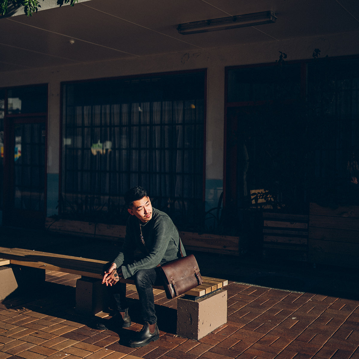 Man sitting on a bench after work with his work satchel on.