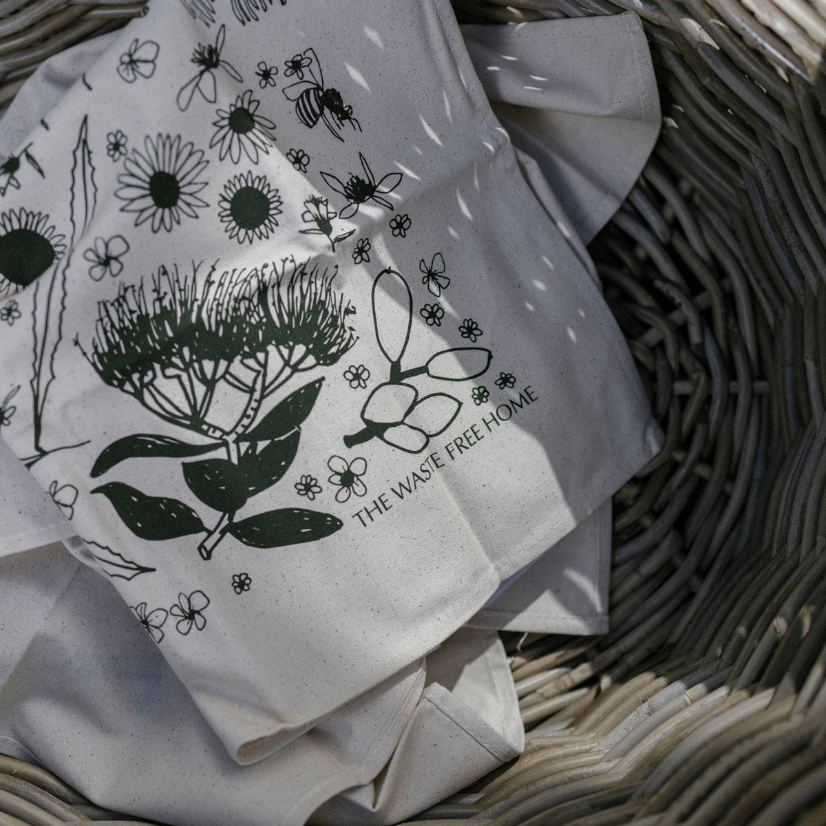 Wicker basket with apples on a wooden surface next to folded fabric with nature-themed design