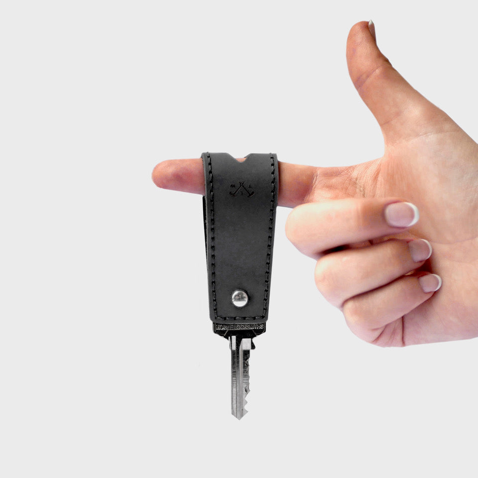 Hand holding a black leather key fob against a light gray background