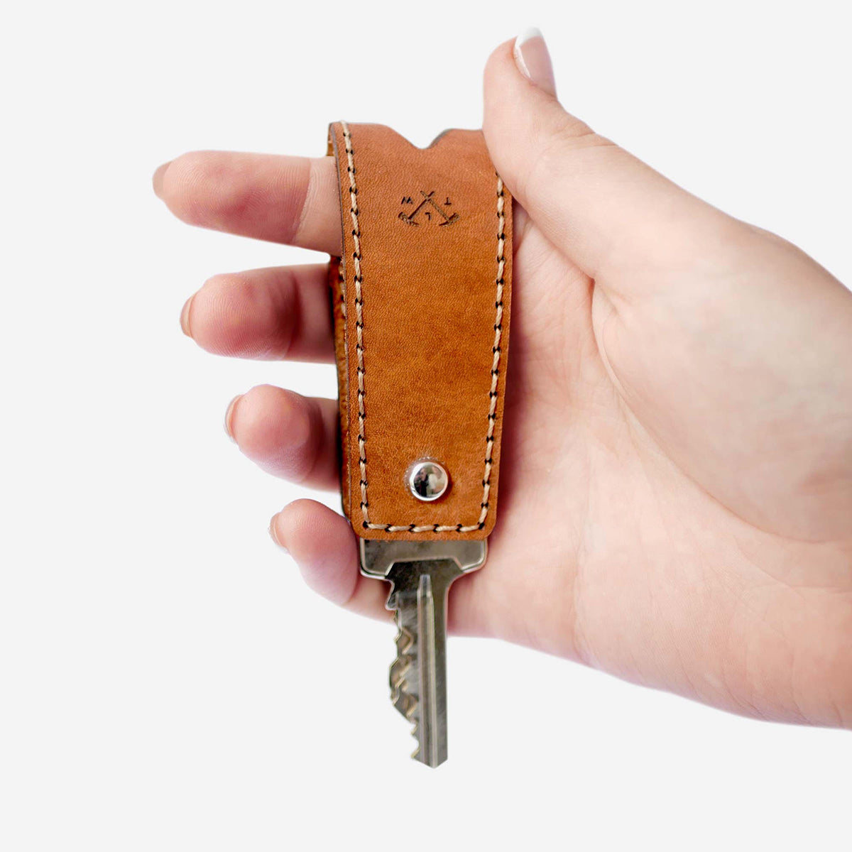 Hand holding a brown leather key fob with a key on a white background