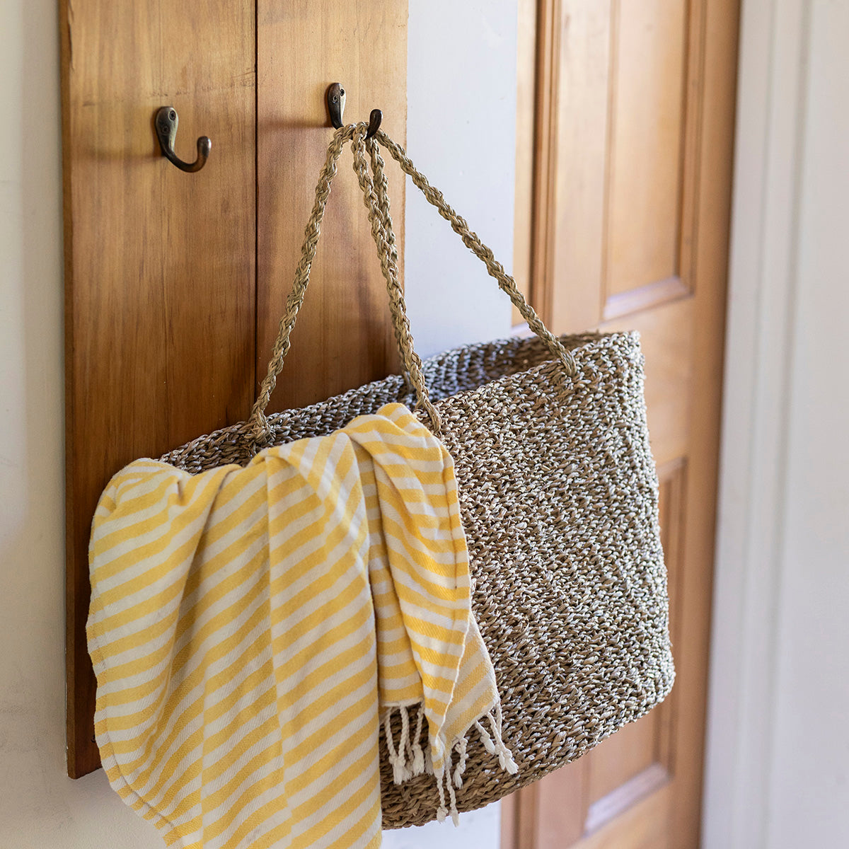 Woven bag with a yellow towel draped over it hanging on a wooden door.