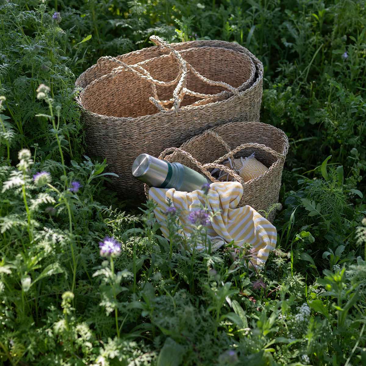 Woven baskets and a bottle in a grassy field with wildflowers