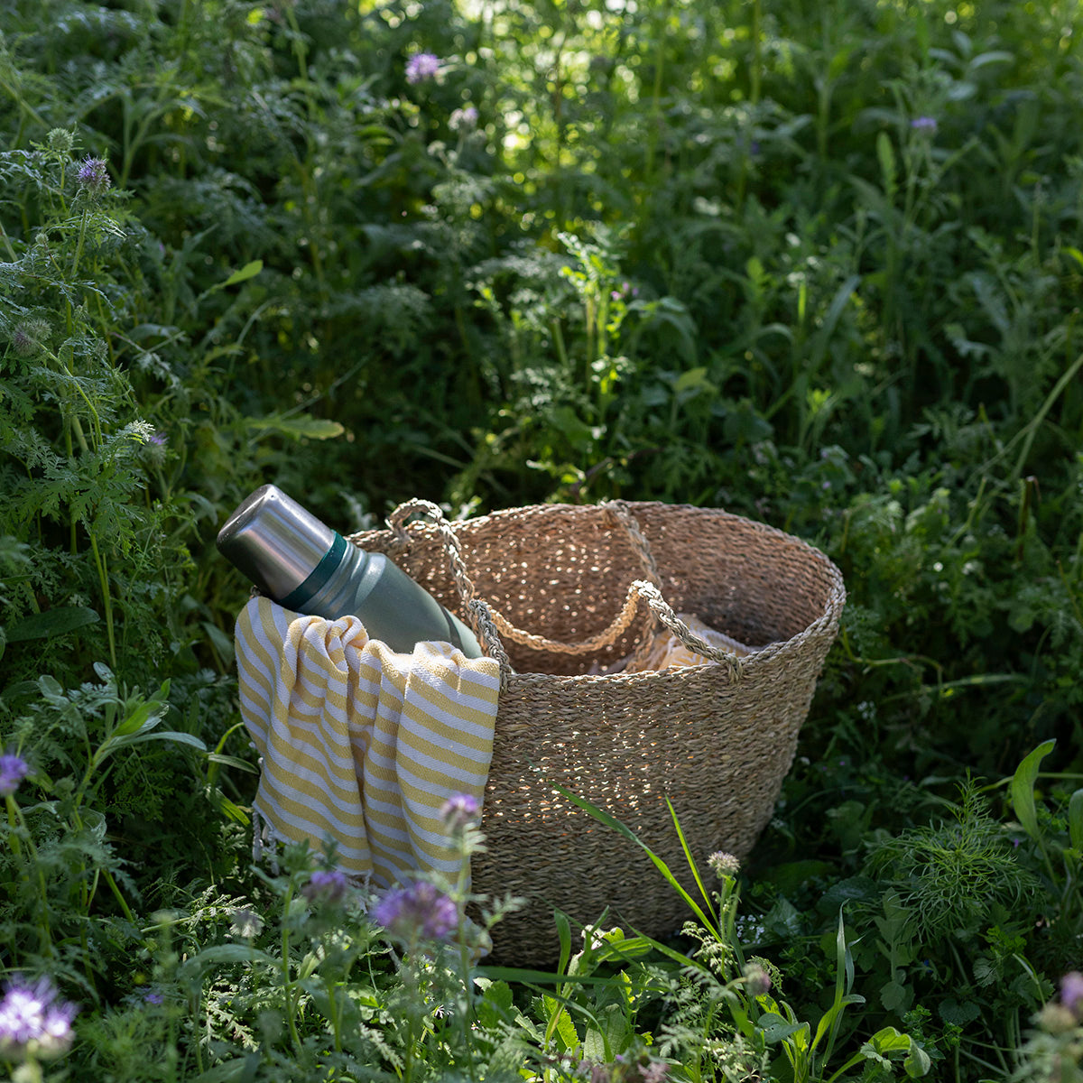 Wicker basket, striped towel, and thermos in a grassy field