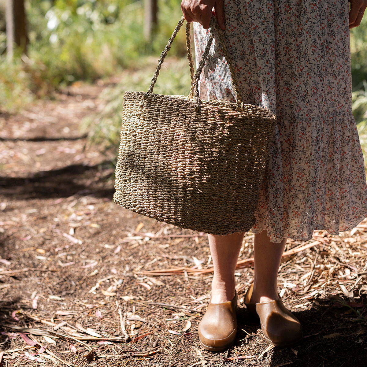 Person holding a woven seagrass marker bag in a natural setting