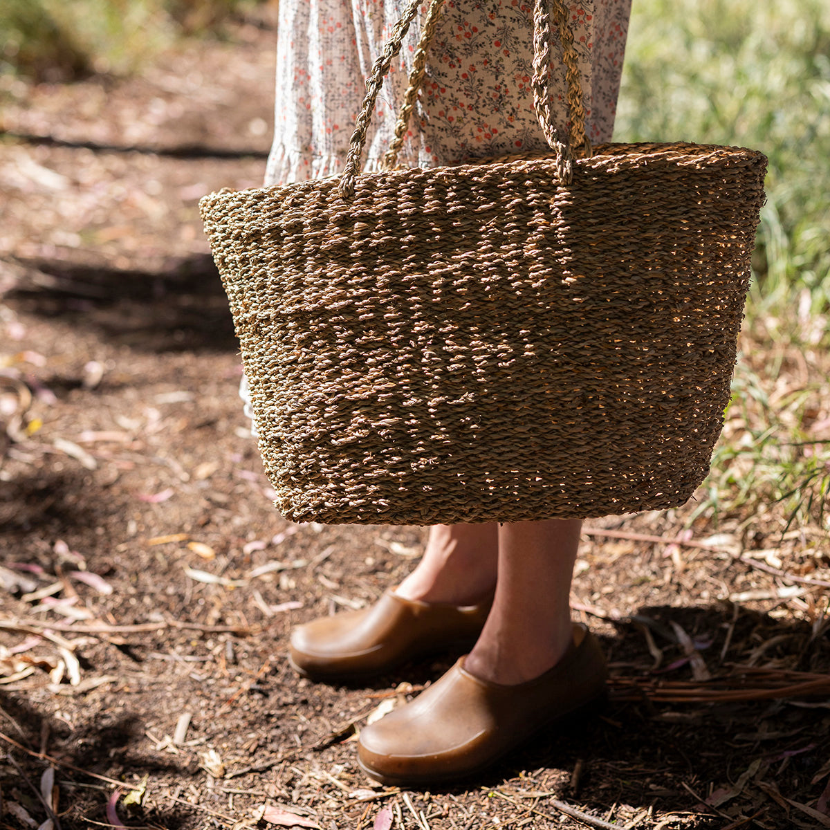 Person holding a woven basket outdoors on a natural path
