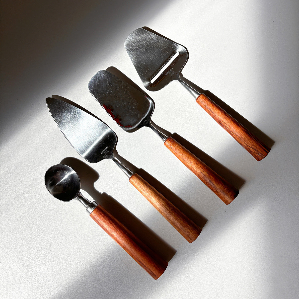 Set of four metal utensils with wooden handles on a reflective surface