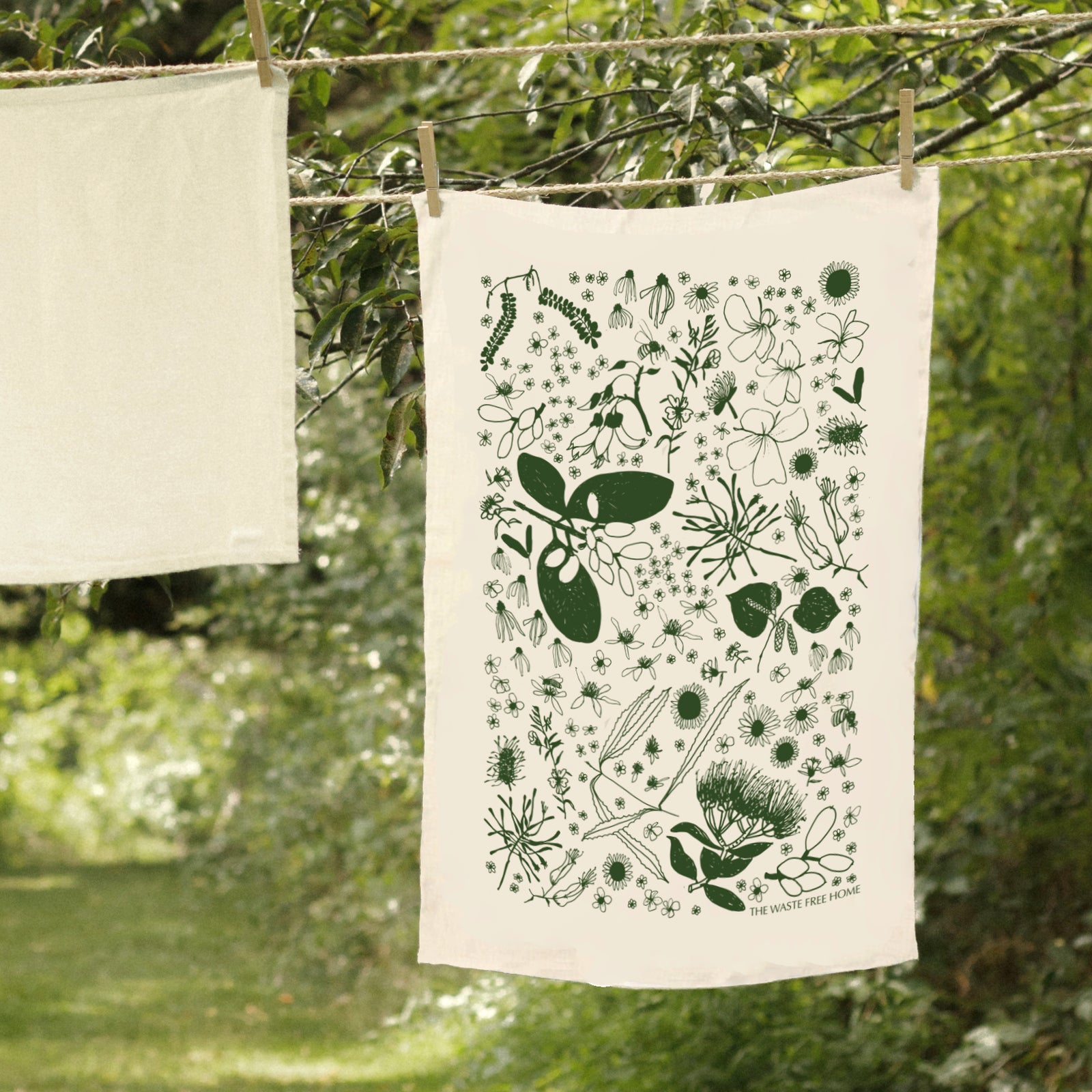 A tea towel with a green floral hand-drawn print hanging on a clothesline outdoors.