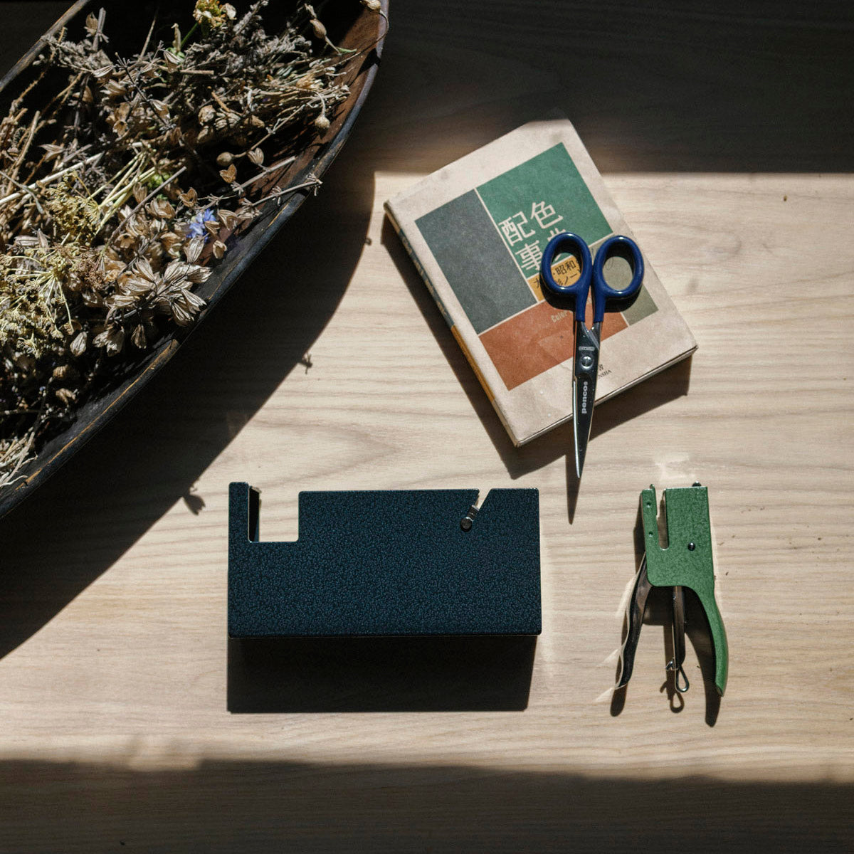 Desk organizer with scissors, stapler, and small book on a wooden surface.