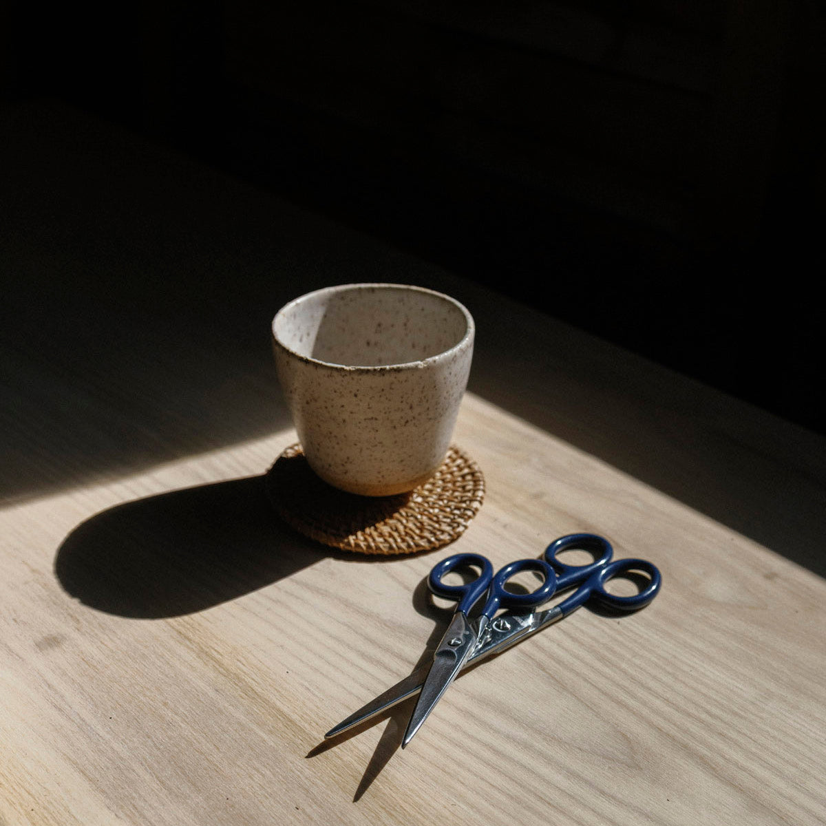 Ceramic cup on a wooden surface with a pair of scissors beside it.