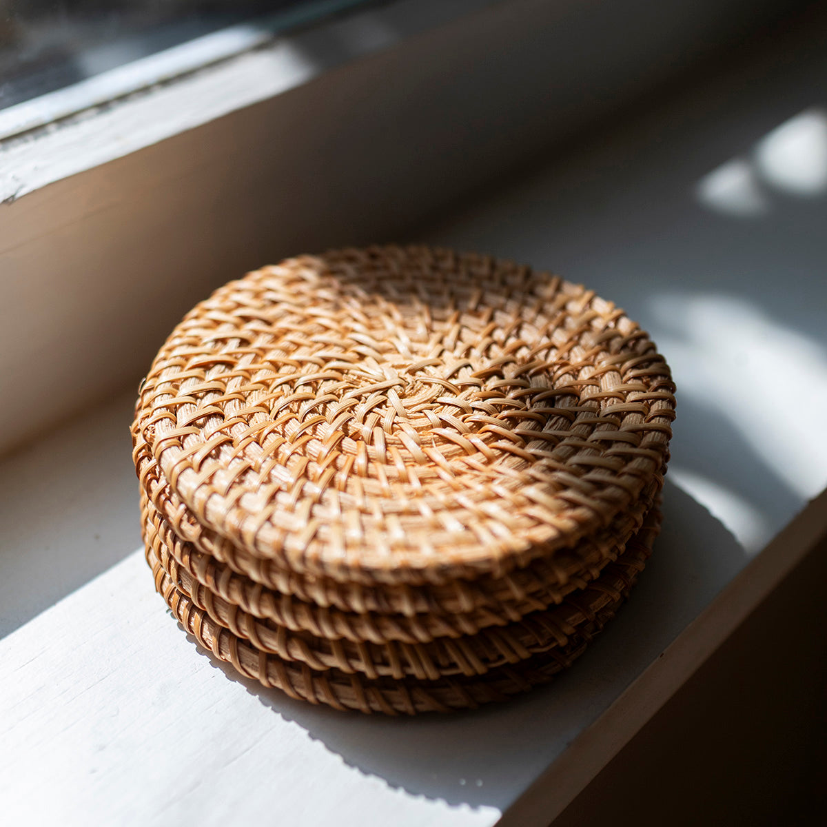 Stack of woven coasters on a light surface with natural light casting shadows.