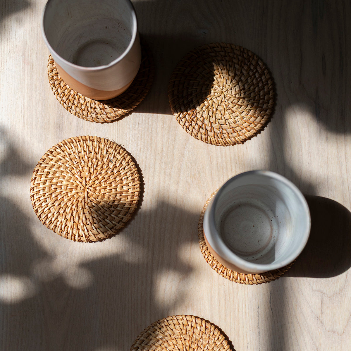 Two cups on round woven coasters on a light wooden surface