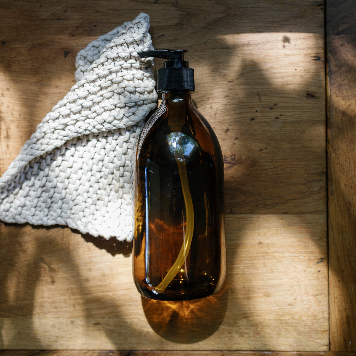 Brown glass bottle with black pump on a wooden surface with a white cloth