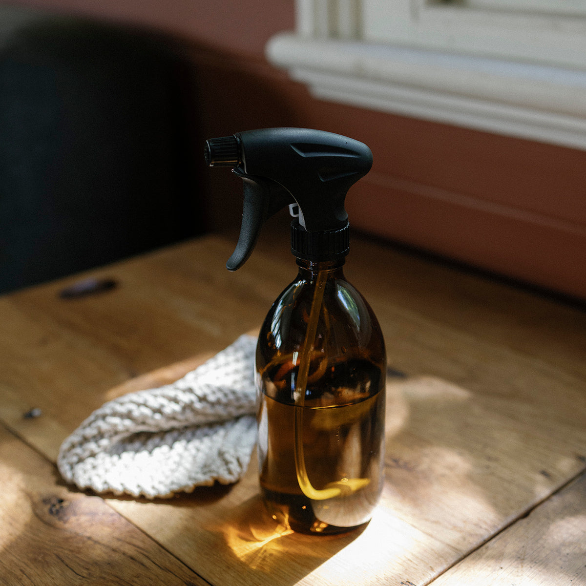Clear reusable Amber spray bottle with black nozzle on a wooden surface