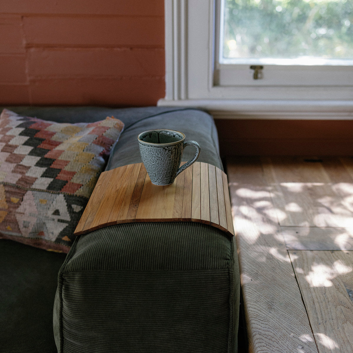 Cup on a wooden sofa armrest tray on a sofa with a window in the background