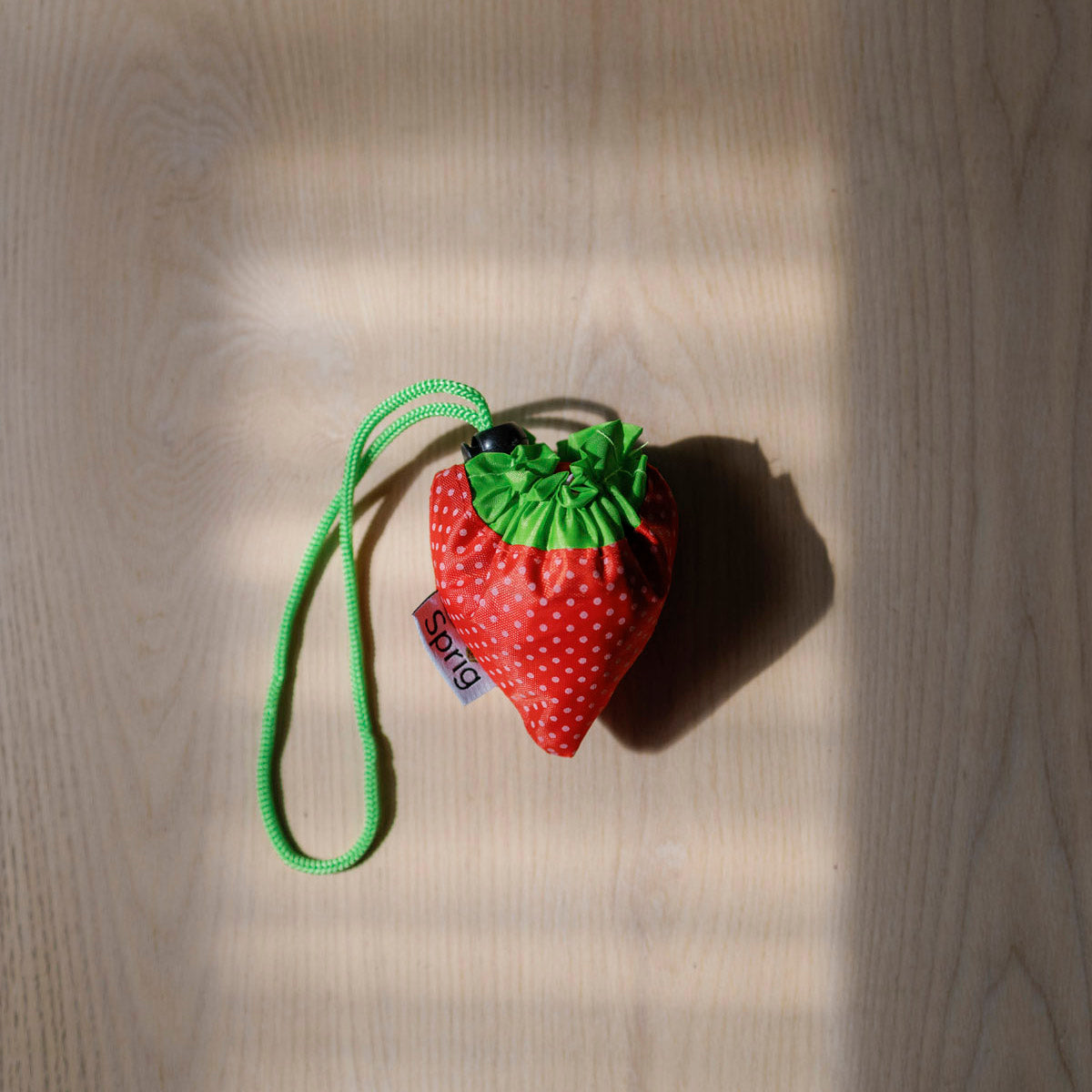 Red strawberry-shaped pouch that folds out into a bag with a green strap on a wooden floor