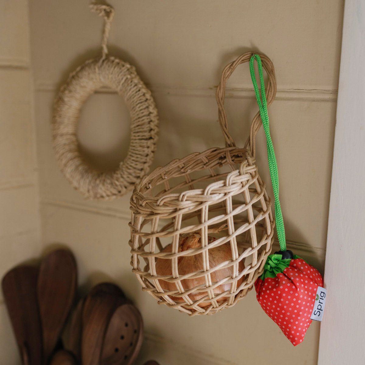 Woven basket with a strawberry-shaped reusable bag hanging on a tiled wall.