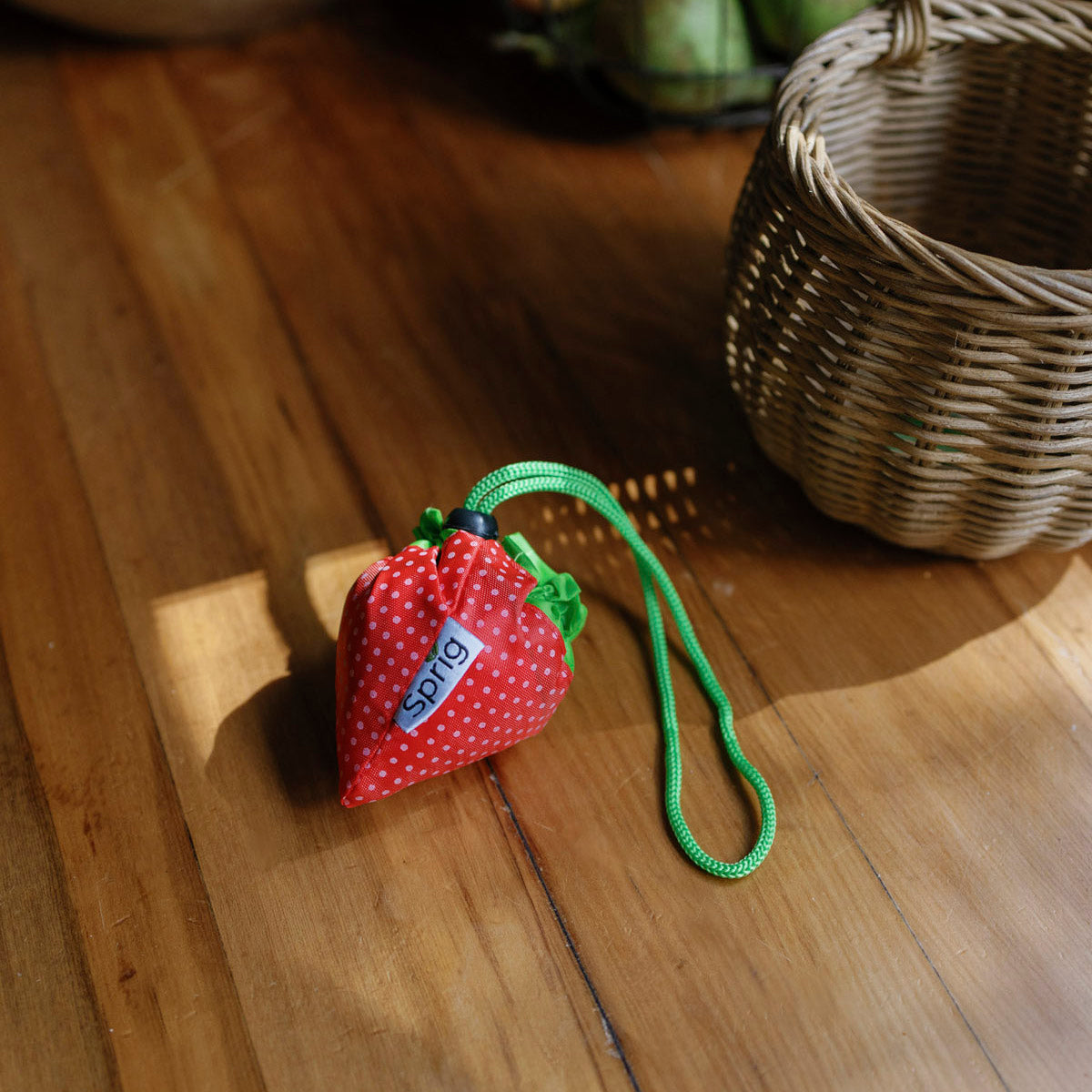 Red strawberry-shaped pouch that folds out into a bag with a green strap on a wooden floor