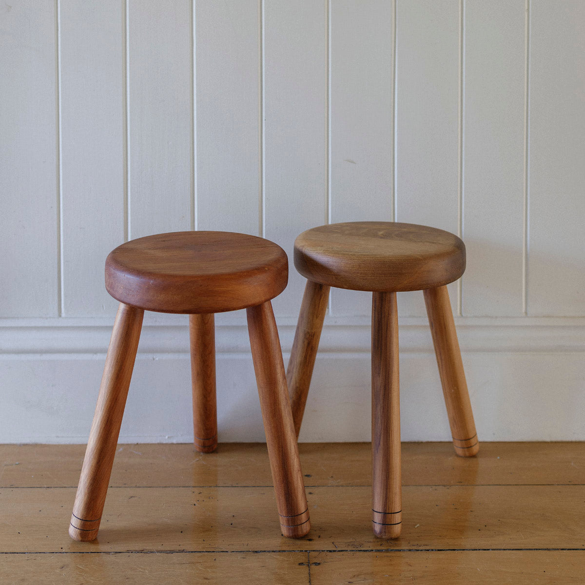 Two wooden stools against a white paneled wall.
