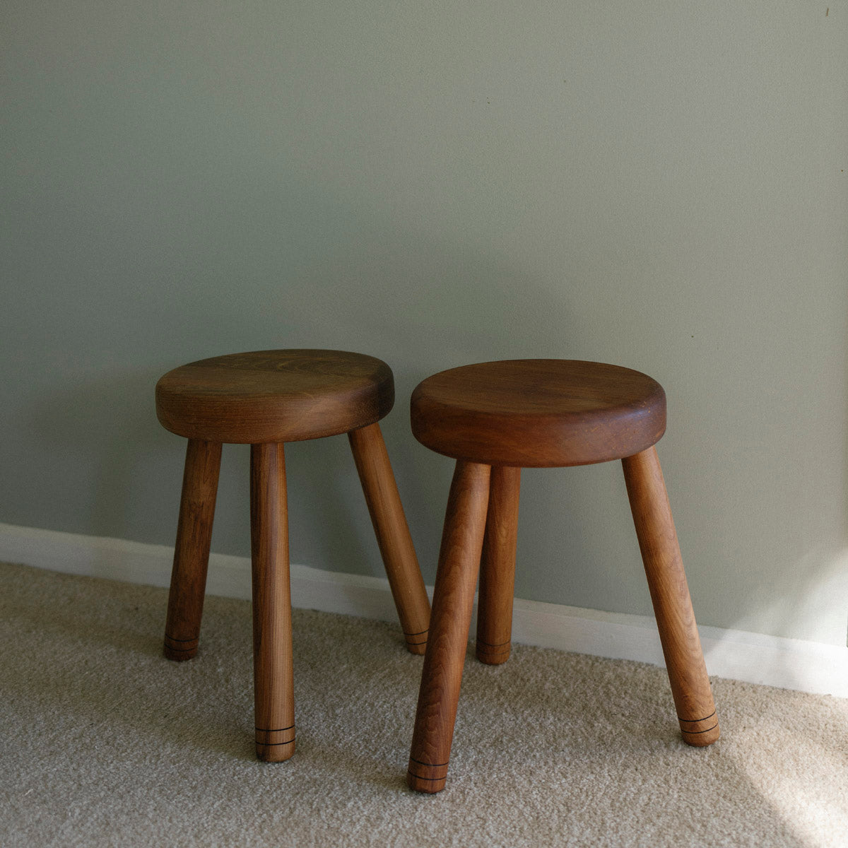 Two wooden stools against a plain wall.